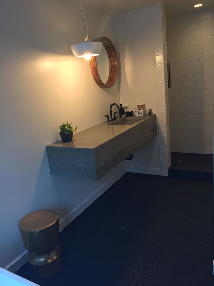Modern bathroom with concrete sink, gold stool, round mirror, and black floor.