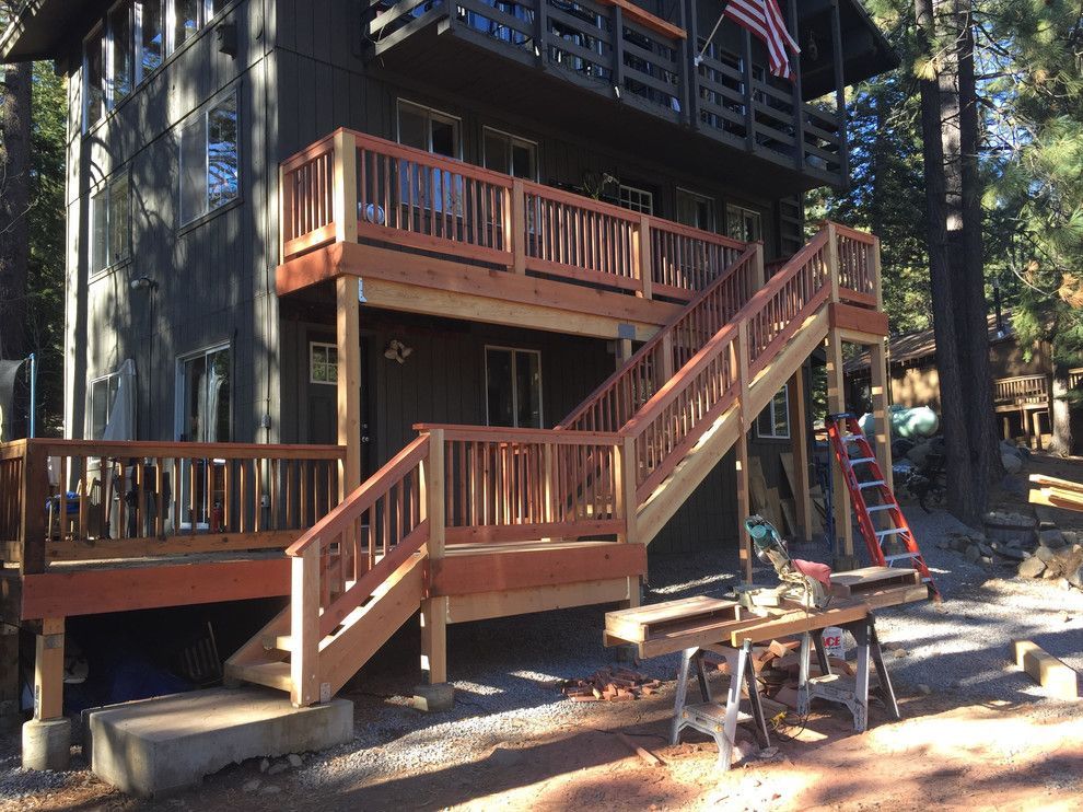 Wooden deck and stairs on a two-story house, redwood color. Outdoor setting, construction tools visible.