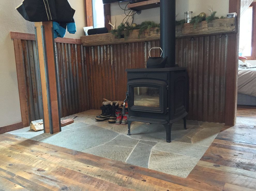 Cozy room with wood-burning stove on stone hearth, corrugated metal backdrop, and rustic wood flooring.