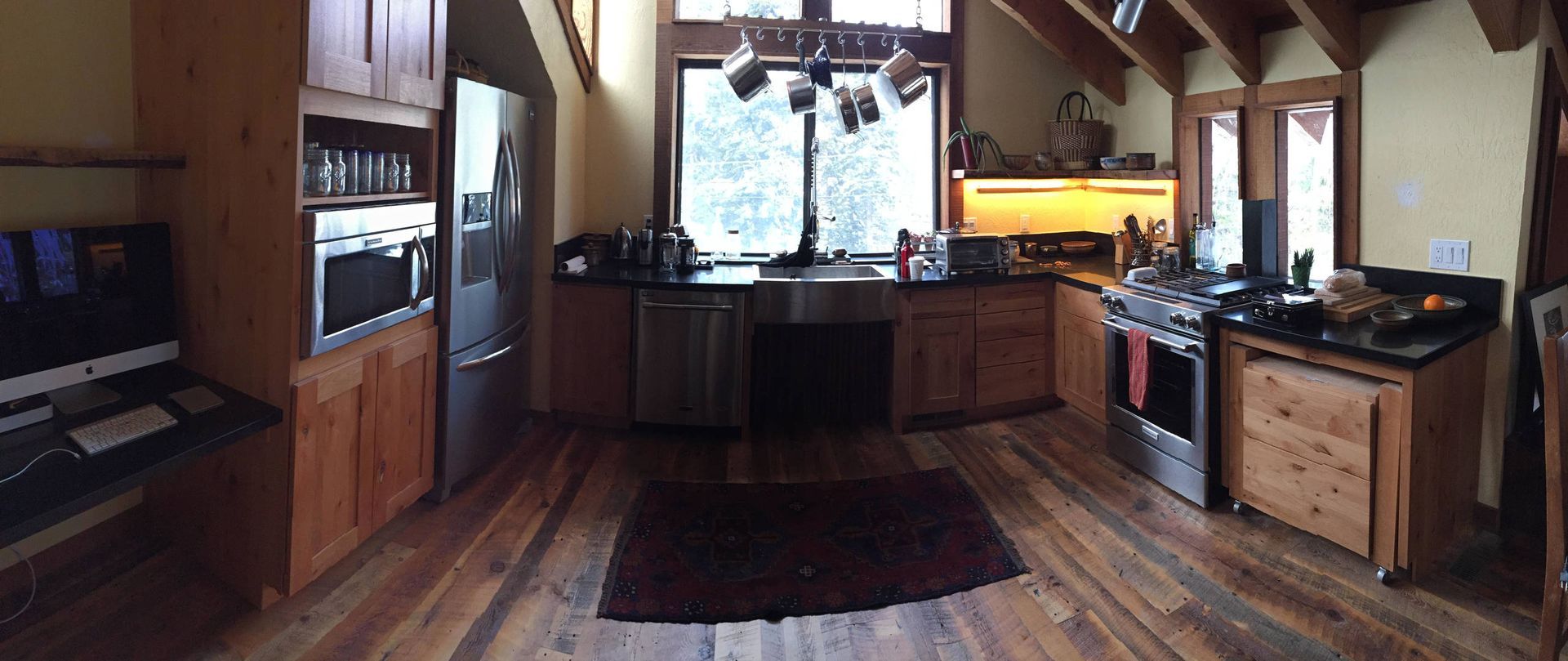 Kitchen with wooden cabinets, stainless steel appliances, large window, and hardwood floors.