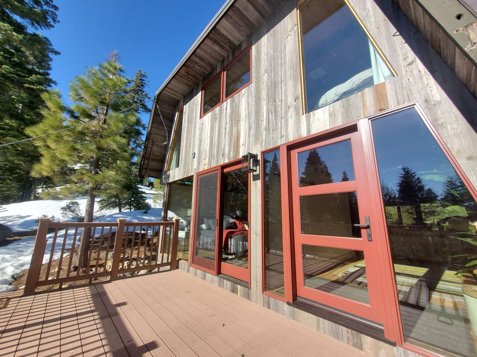 A-frame cabin exterior with red doors and large windows, surrounded by a deck and snow.