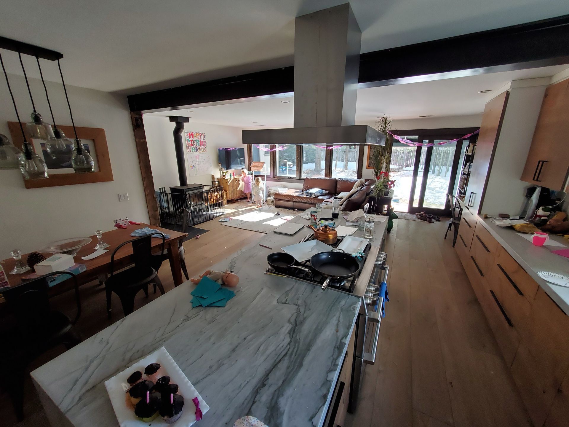 Kitchen with large island, stove, dining table, and view to a living area with a wood stove and windows.
