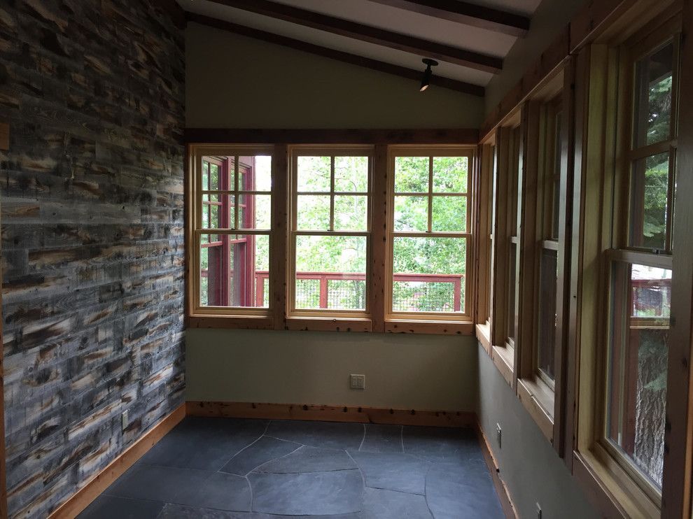 Sunroom with stone wall and windows looking onto trees.