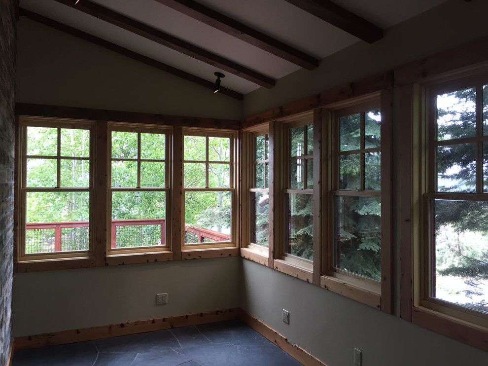 Sunroom with wooden-framed windows, dark floor, stone wall, and exposed wooden beams.