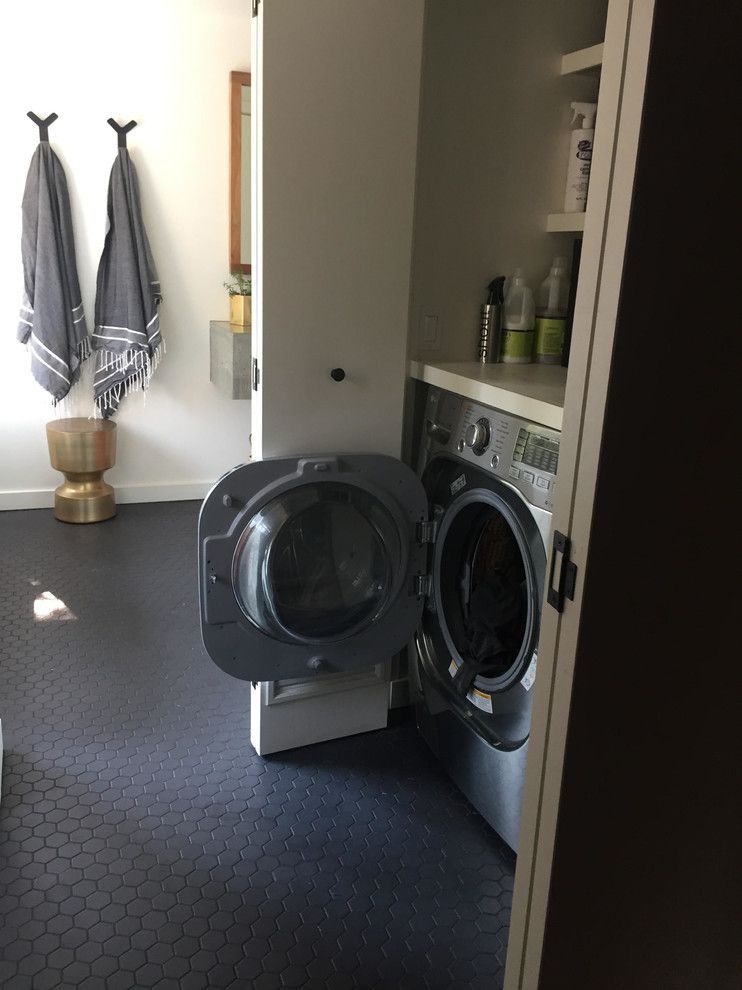 Laundry room with washing machine, door open, and adjacent shelving. Black tiled floor, towels hanging.