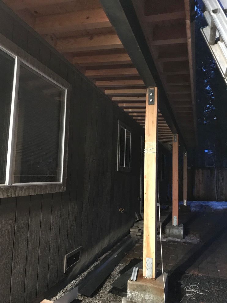 Exterior view of a building with a covered deck supported by wooden posts and a dark siding wall.