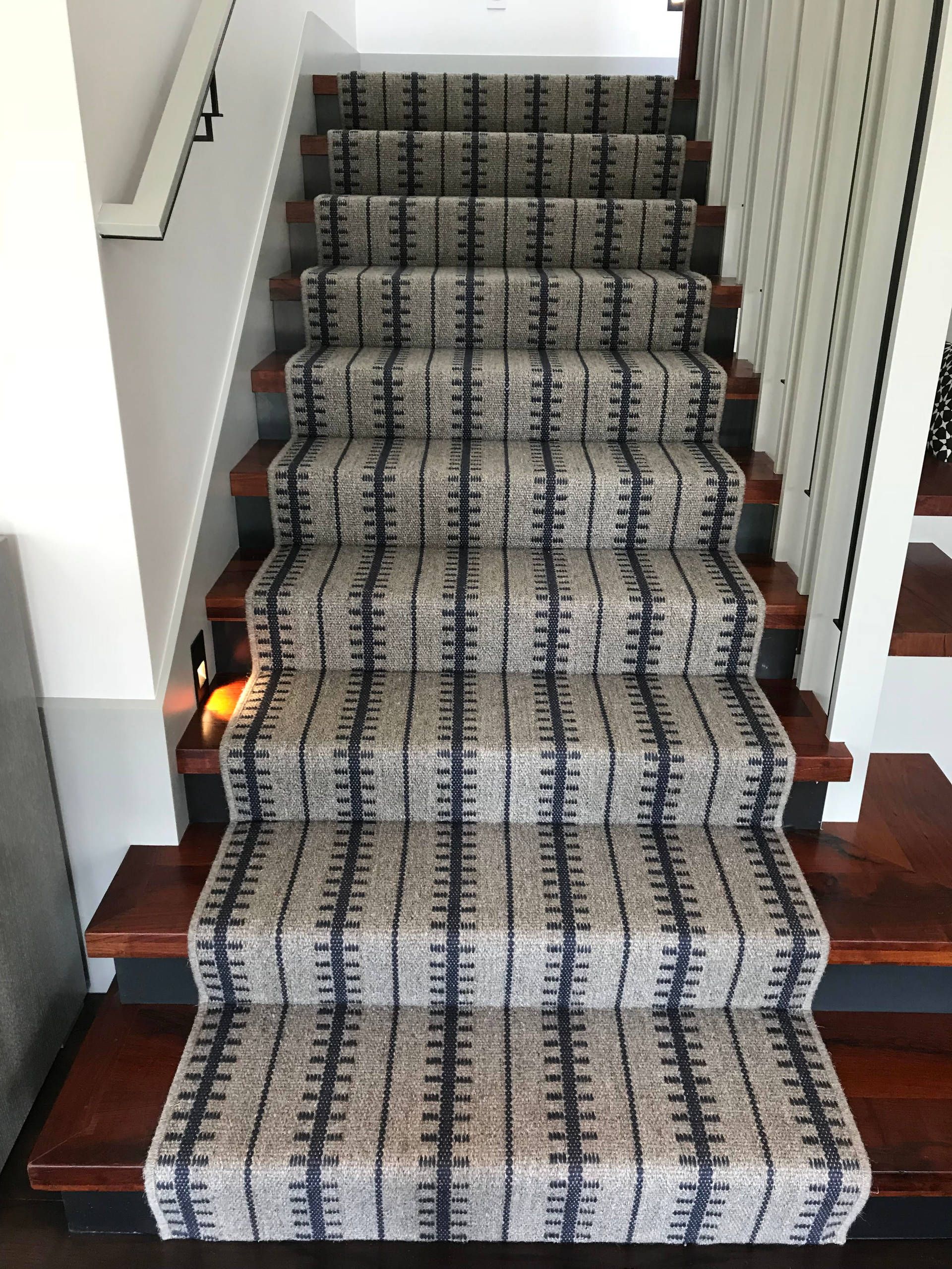 Staircase with carpet runner in a beige and blue pattern, dark wood steps. Handrail on the left.