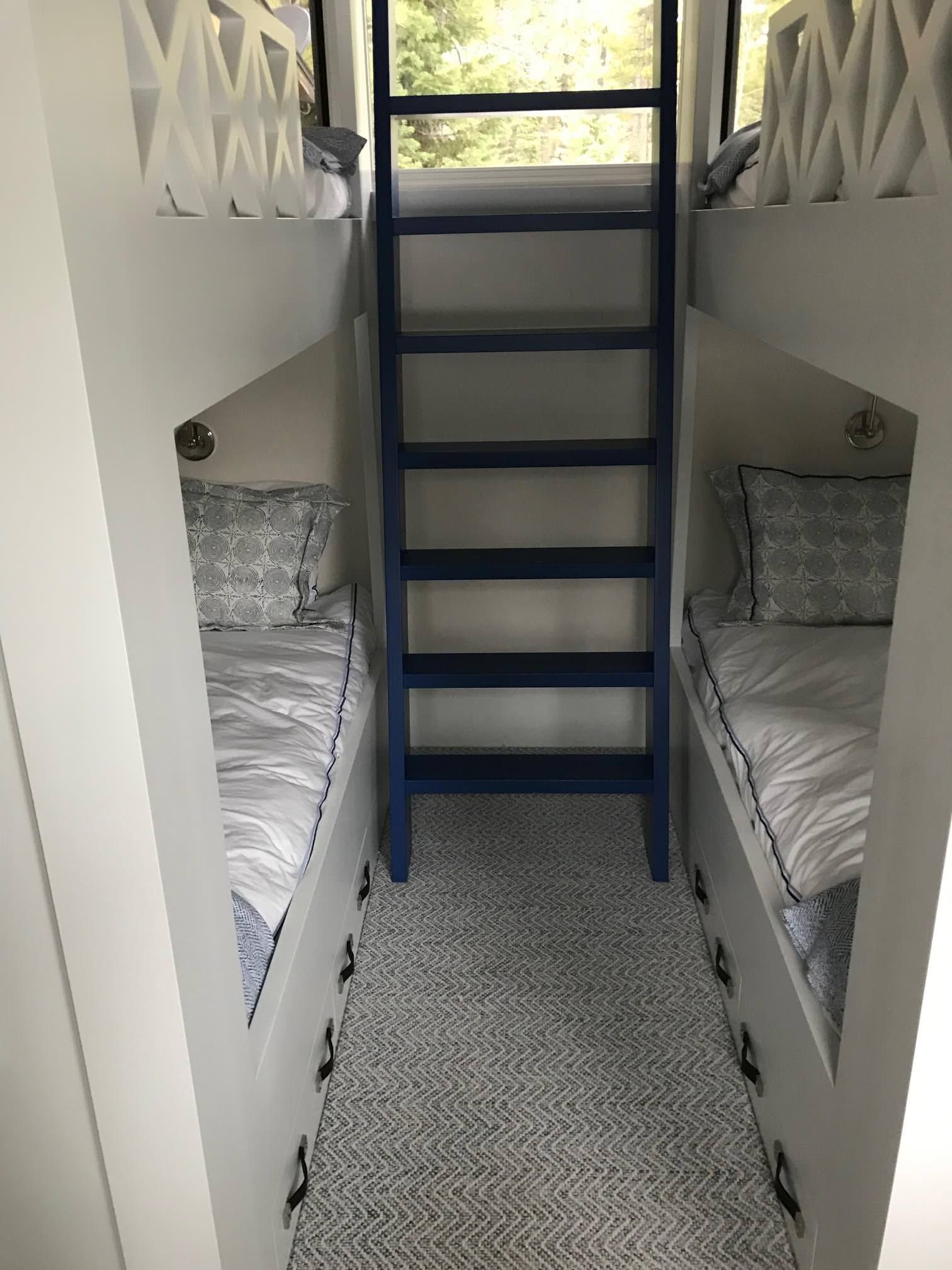 Narrow bedroom with two bunk beds; blue ladder between them. White, gray, and blue color scheme.
