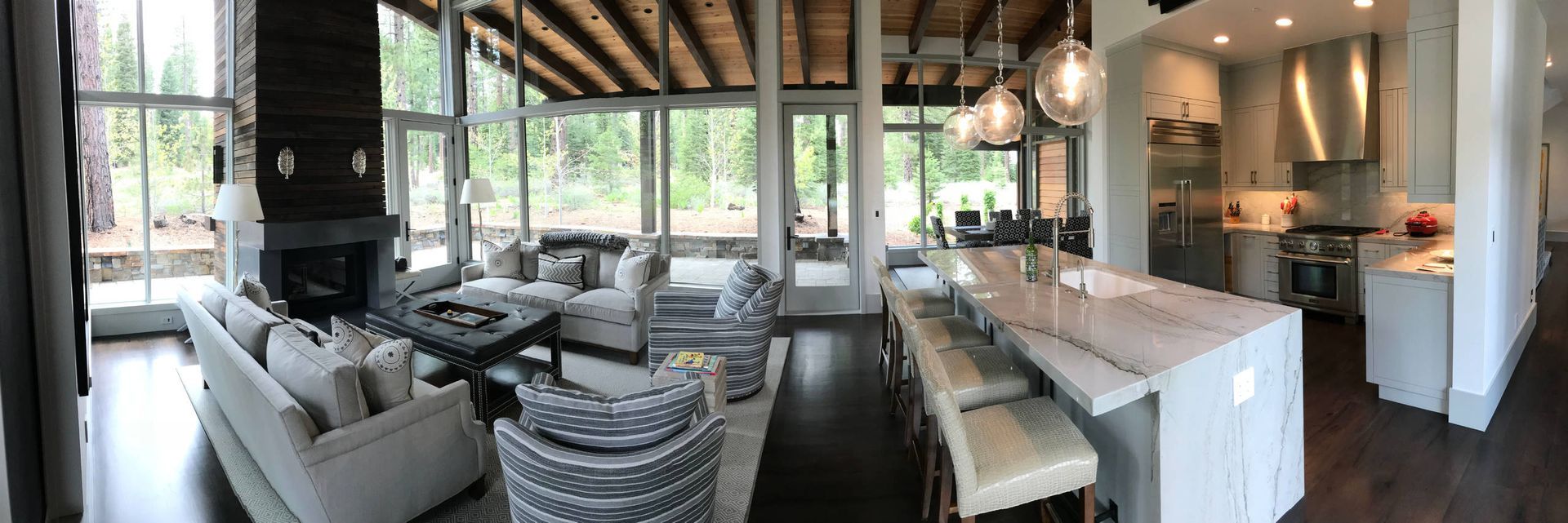 Spacious modern living room with fireplace, kitchen island, and forest view.