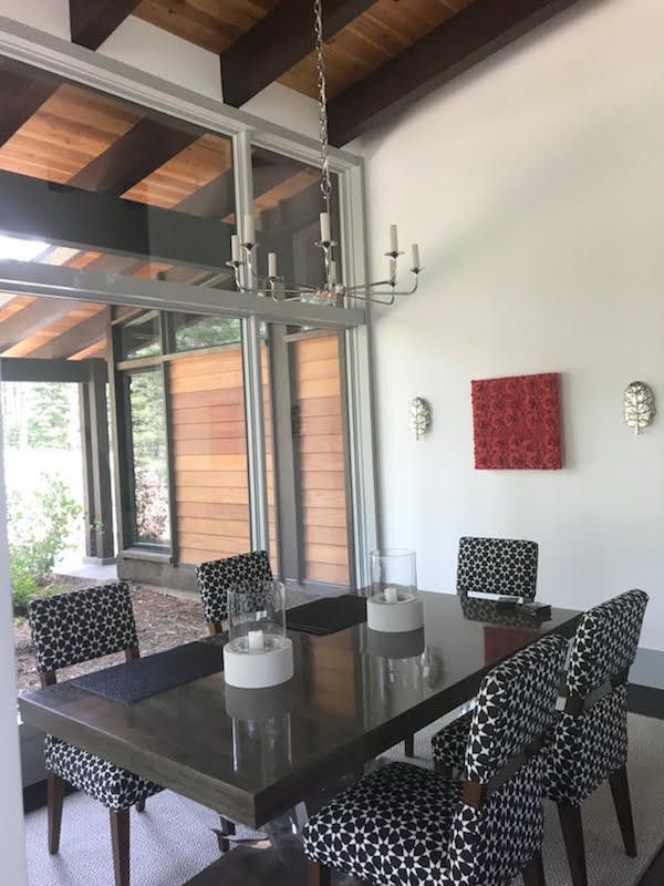 Dining room with a table and patterned chairs, chandelier, artwork, and large windows.