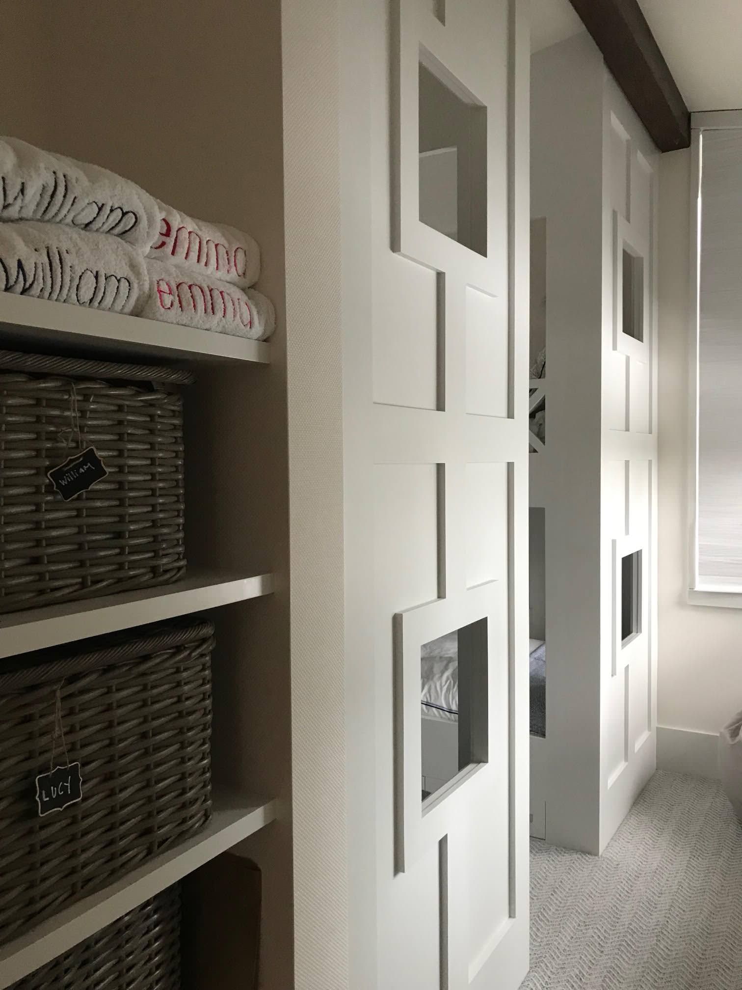 White closet doors with rectangular cutouts, next to shelves with wicker baskets and towels.