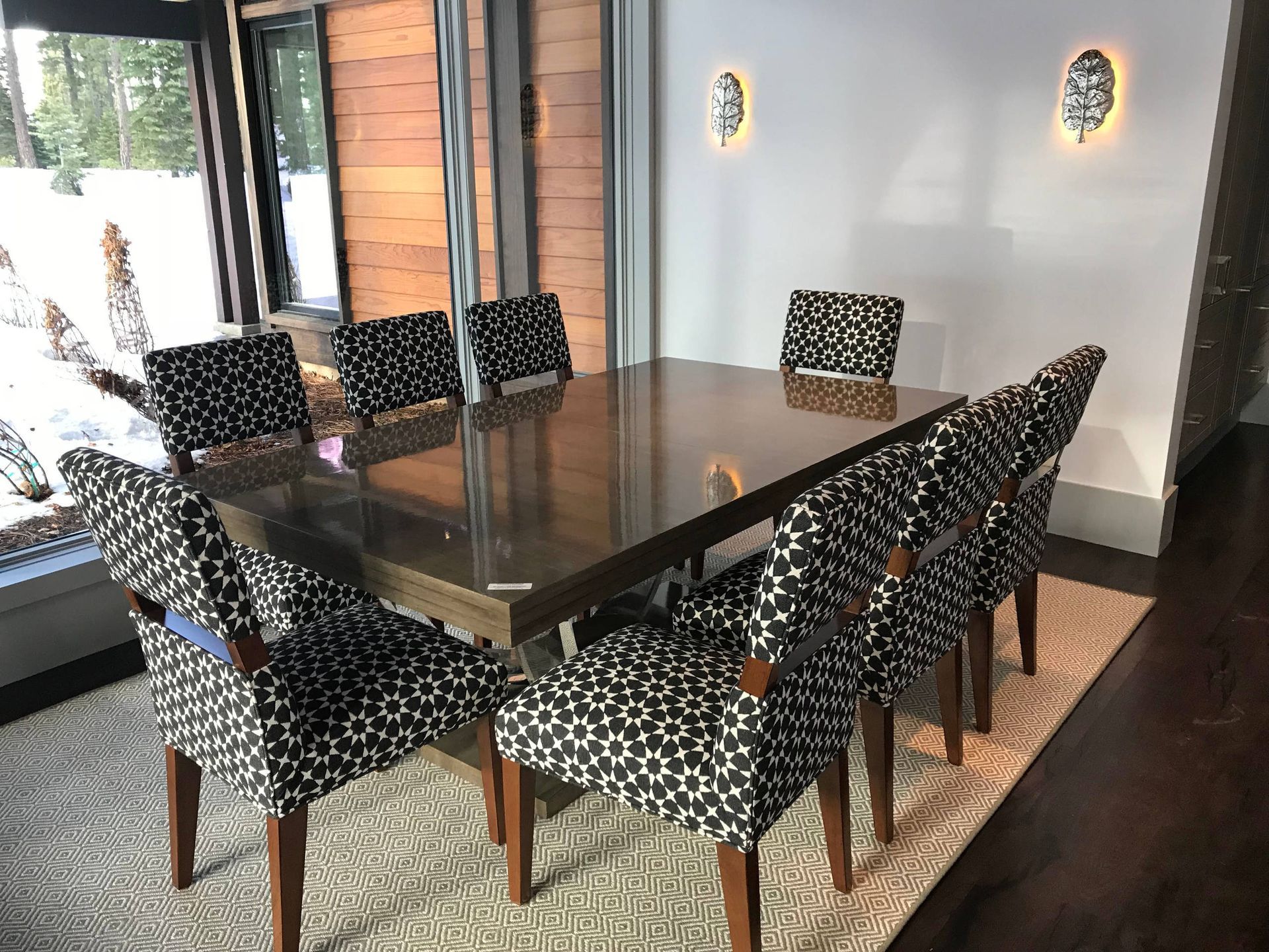 Dining room with a long wooden table, eight patterned chairs, and a window.