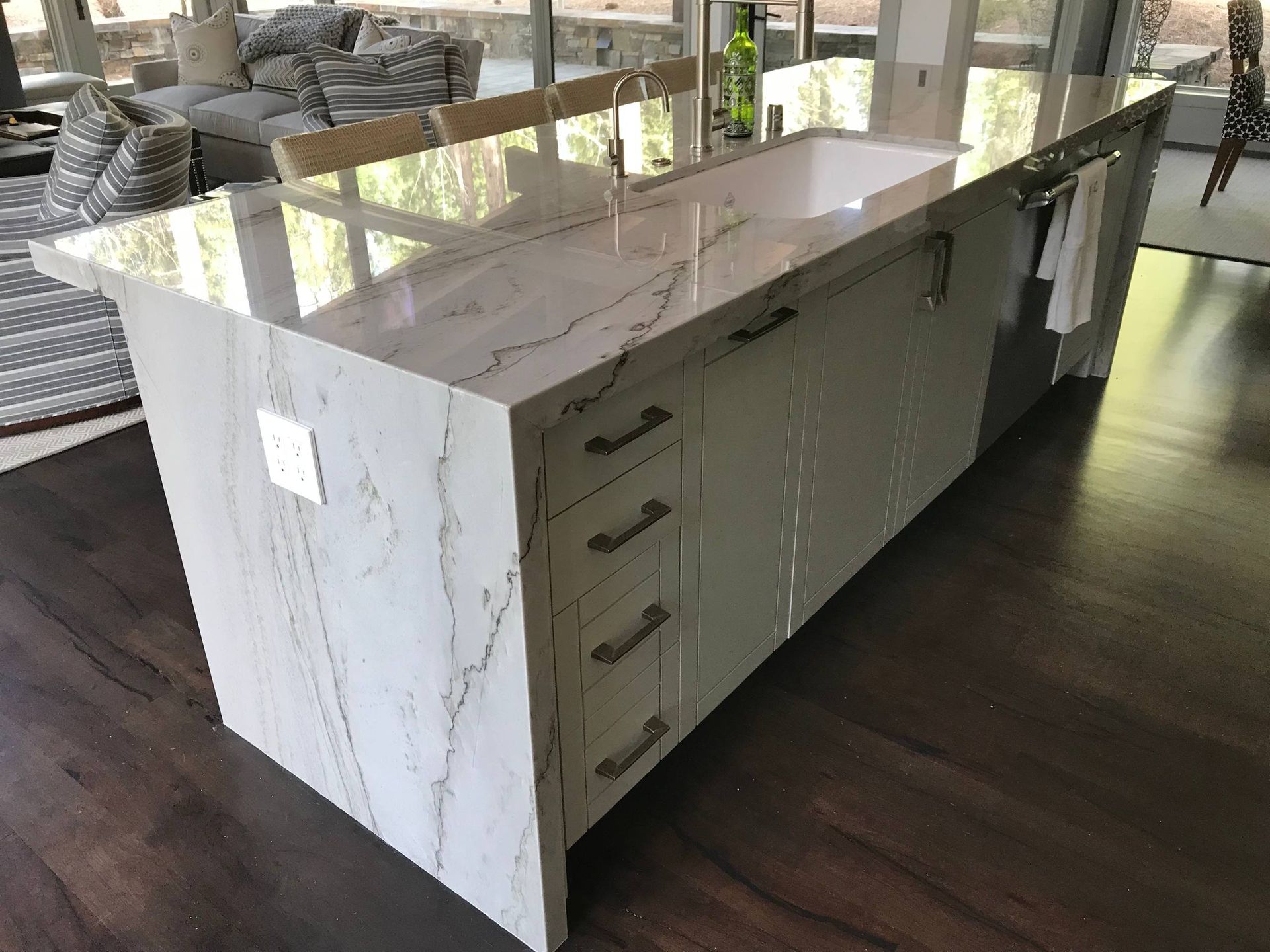 Kitchen island with white marble countertop, drawers, and dark wood floor.