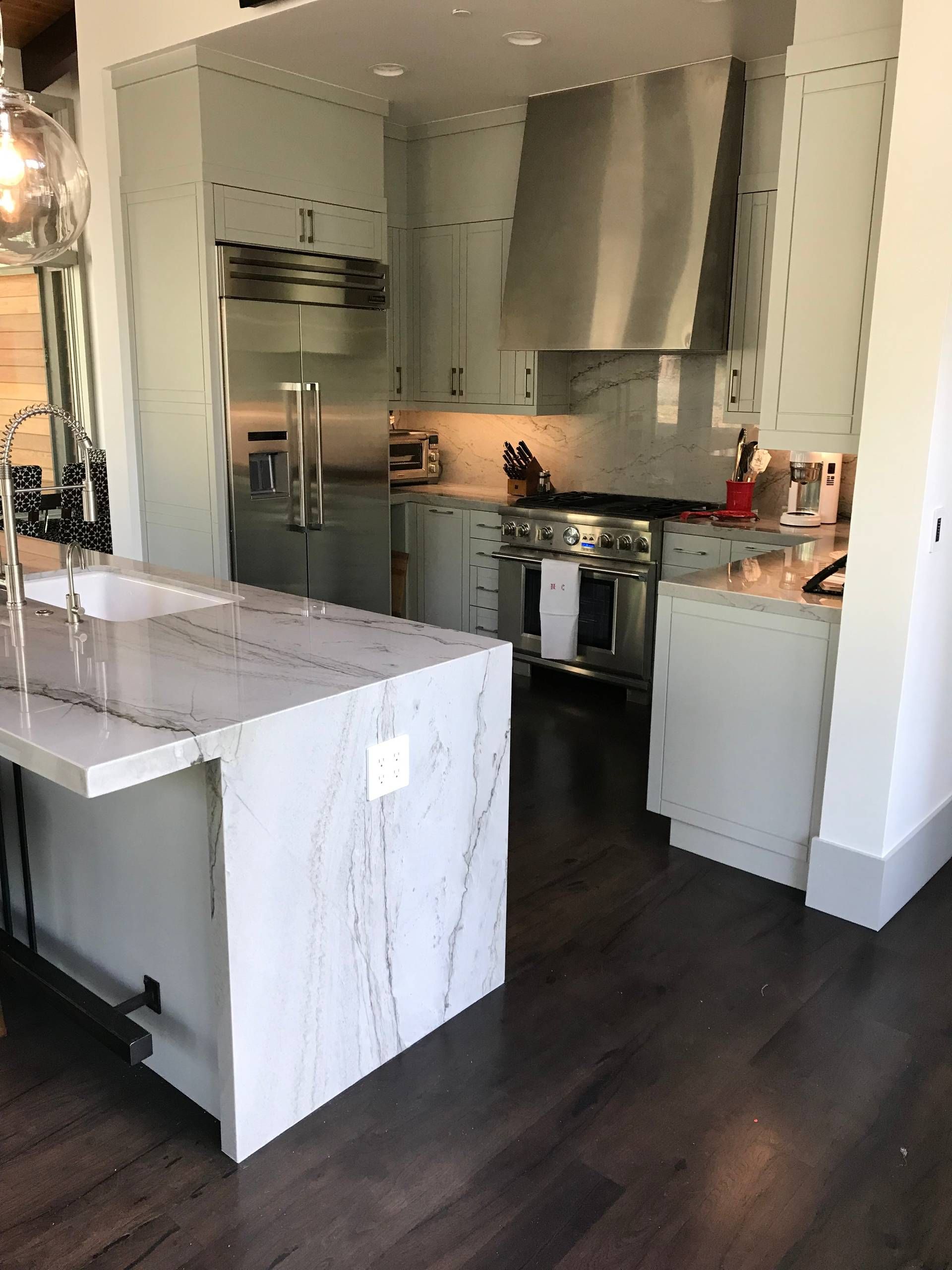 Kitchen with white cabinets, marble island, stainless steel appliances, dark wood floor.