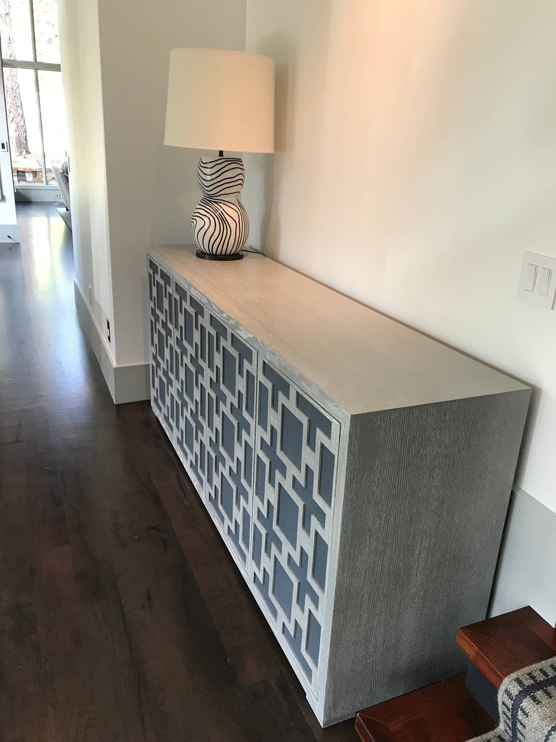Long, gray cabinet with blue and white geometric pattern, lamp on top, in a hallway.