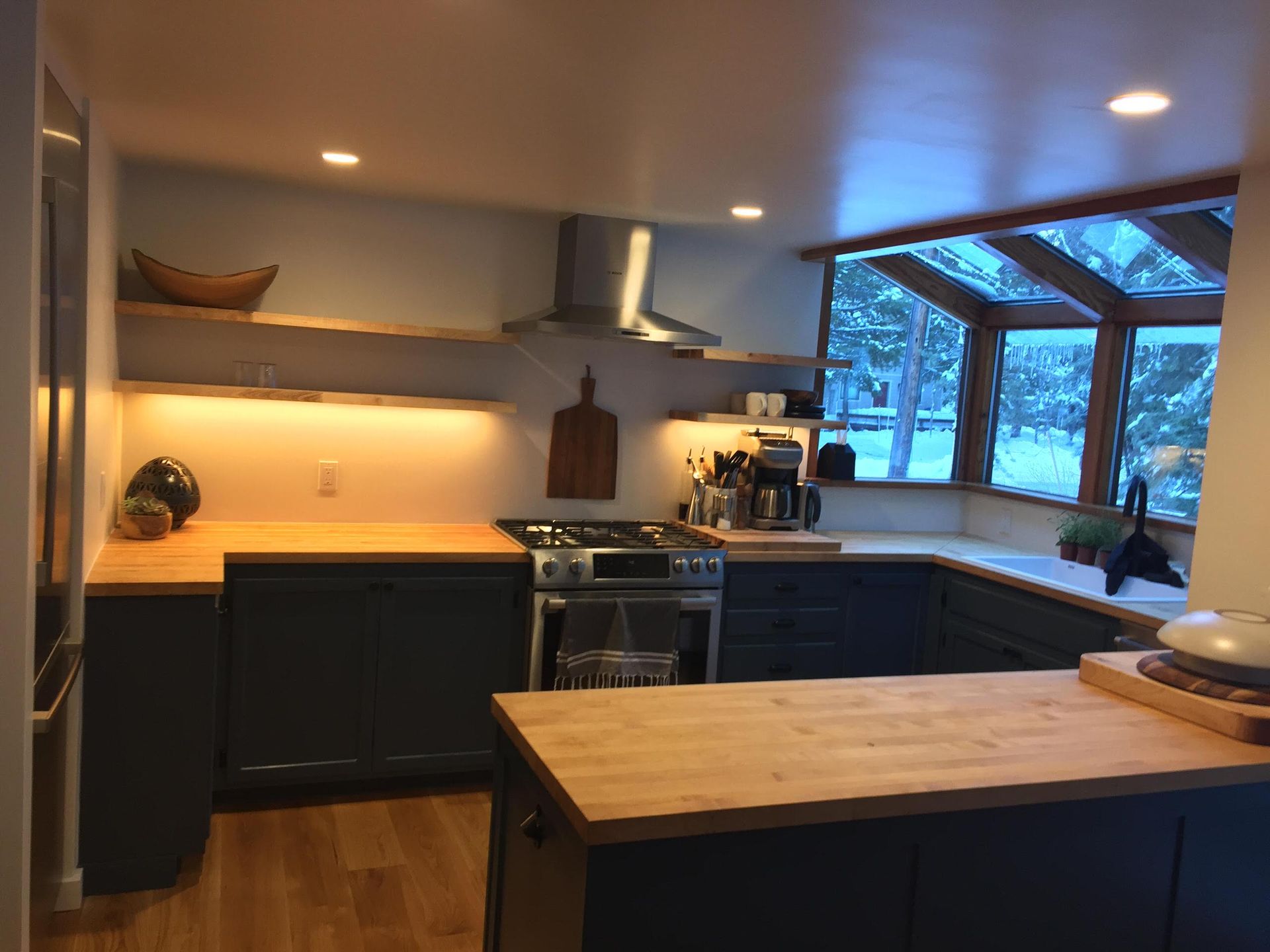 Kitchen with blue cabinets, wood countertops, and large window.