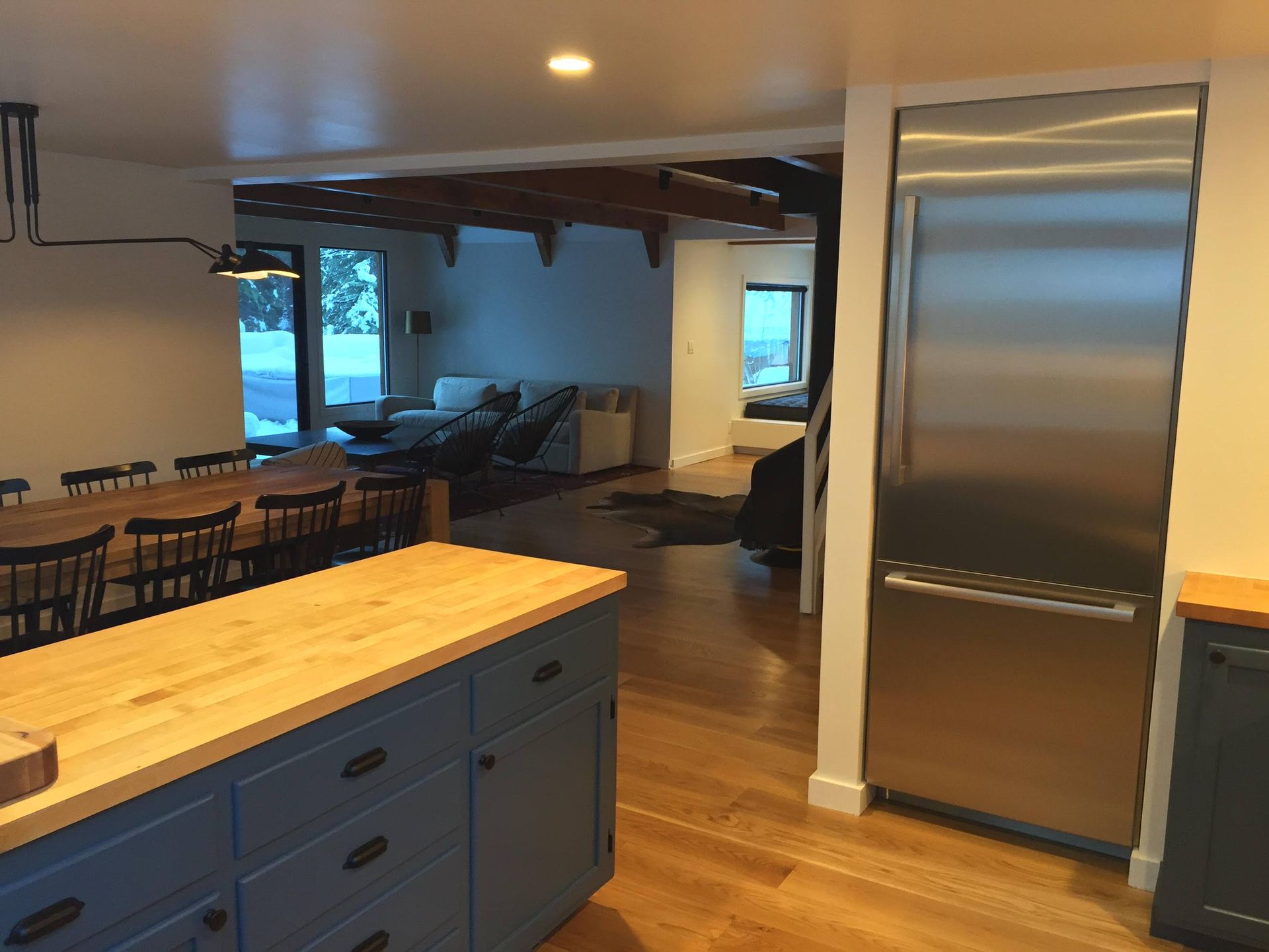 Kitchen with a blue island, wood countertop, large stainless steel refrigerator, and dining table, with living area in the background.