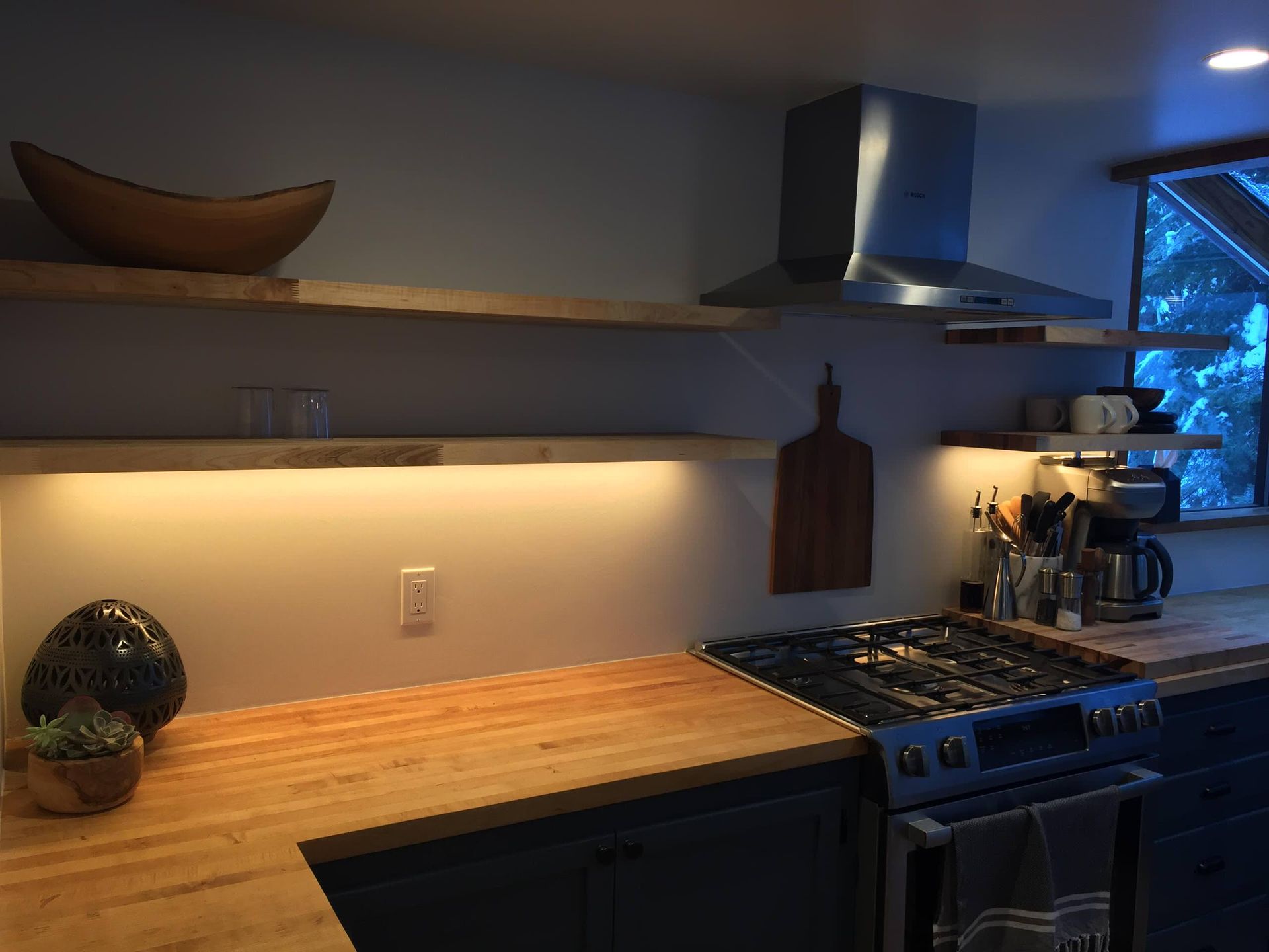Kitchen with butcher block countertops, open shelves, and stainless steel range hood.