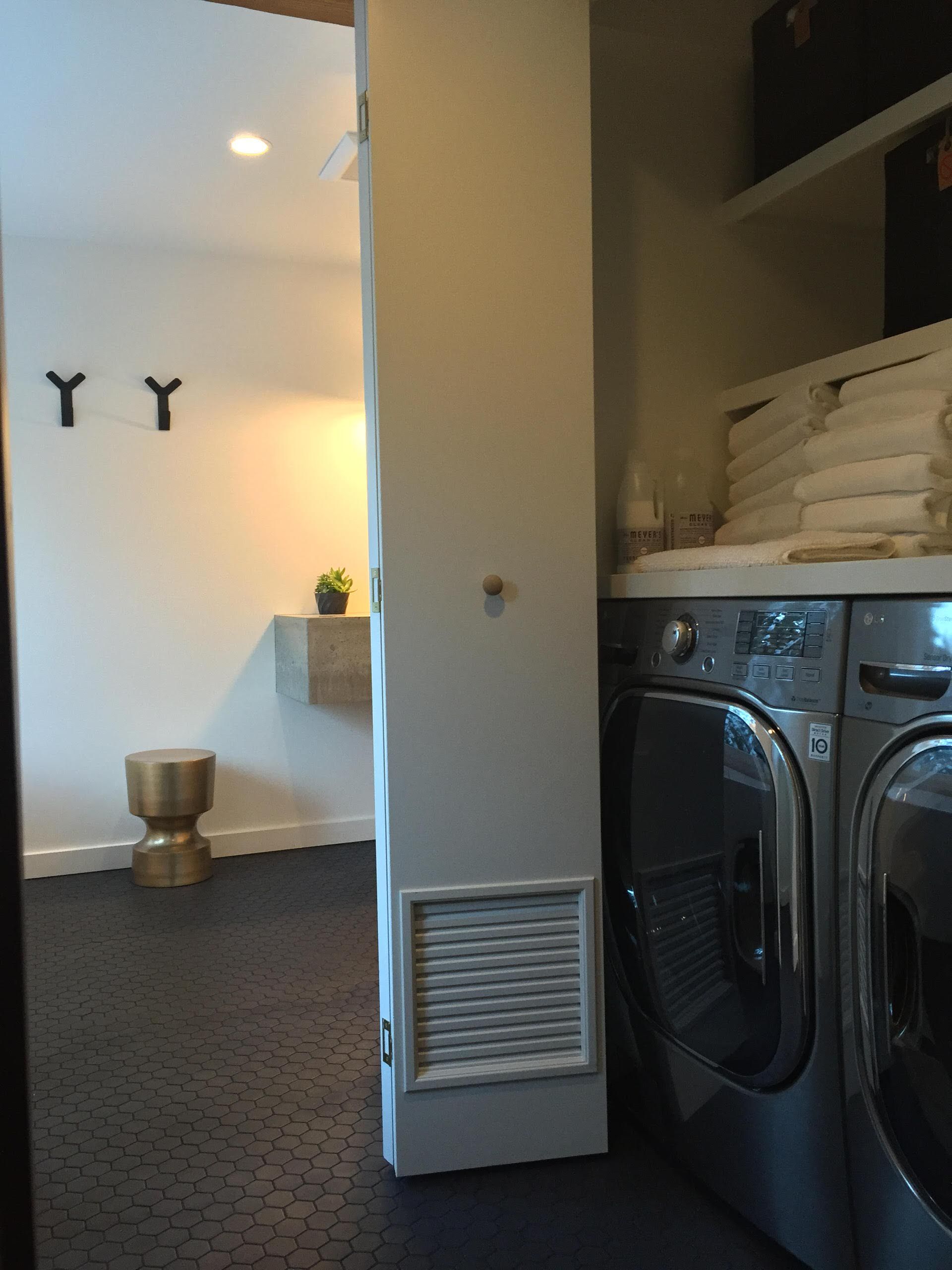 Laundry room with washer, dryer, and doorway leading to a hallway with a stool and coat rack.