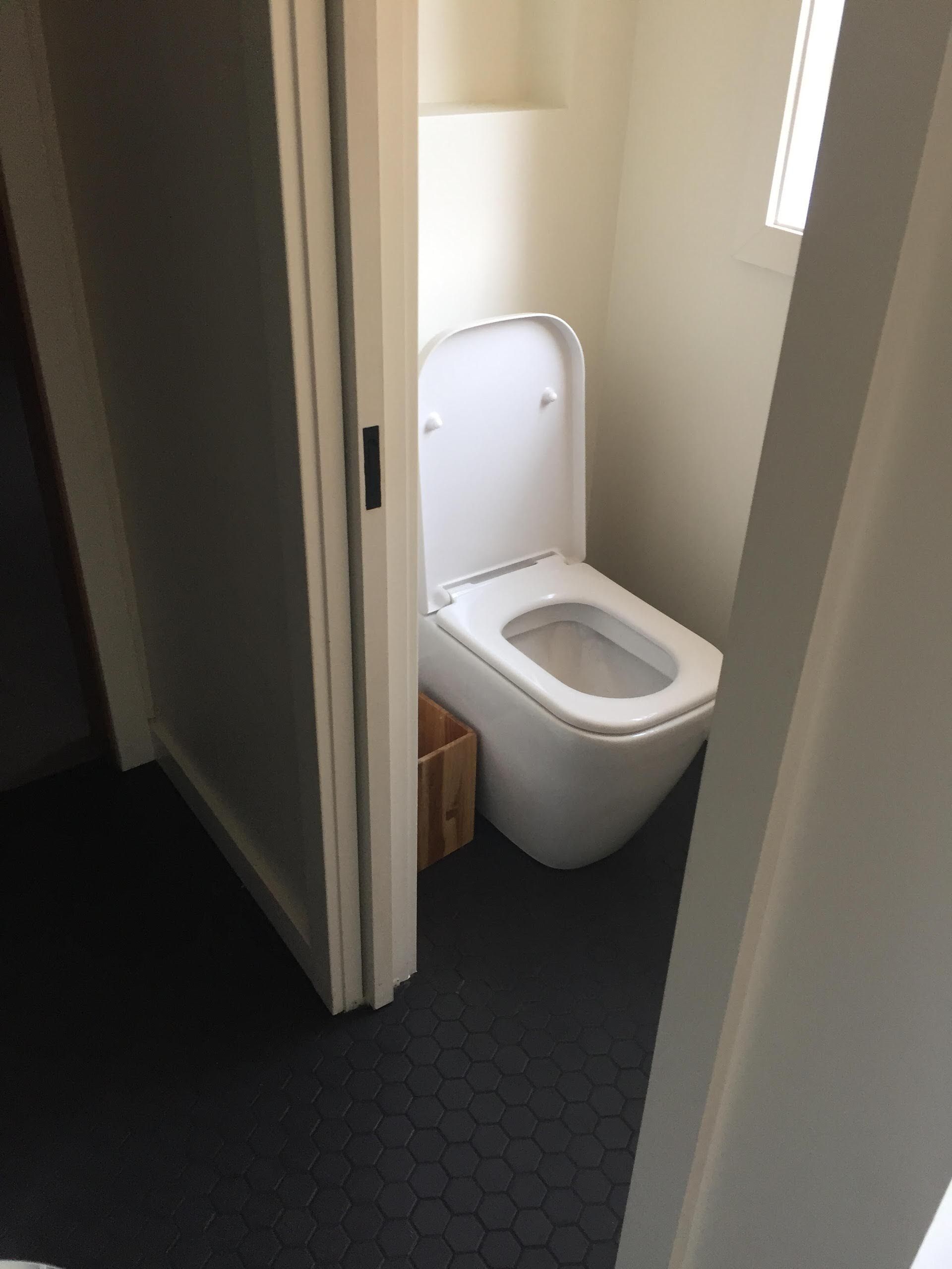 Toilet in a small bathroom with black floor, off-white walls, and a wooden basket.