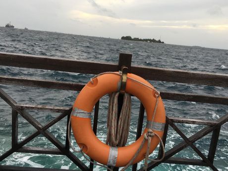 Orange life ring on a railing beside a choppy sea with a small island in the distance