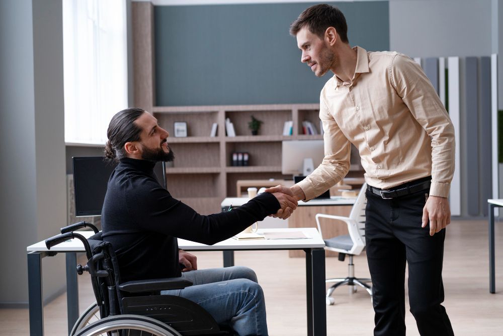 Man in wheelchair shaking hands with standing man in an office setting