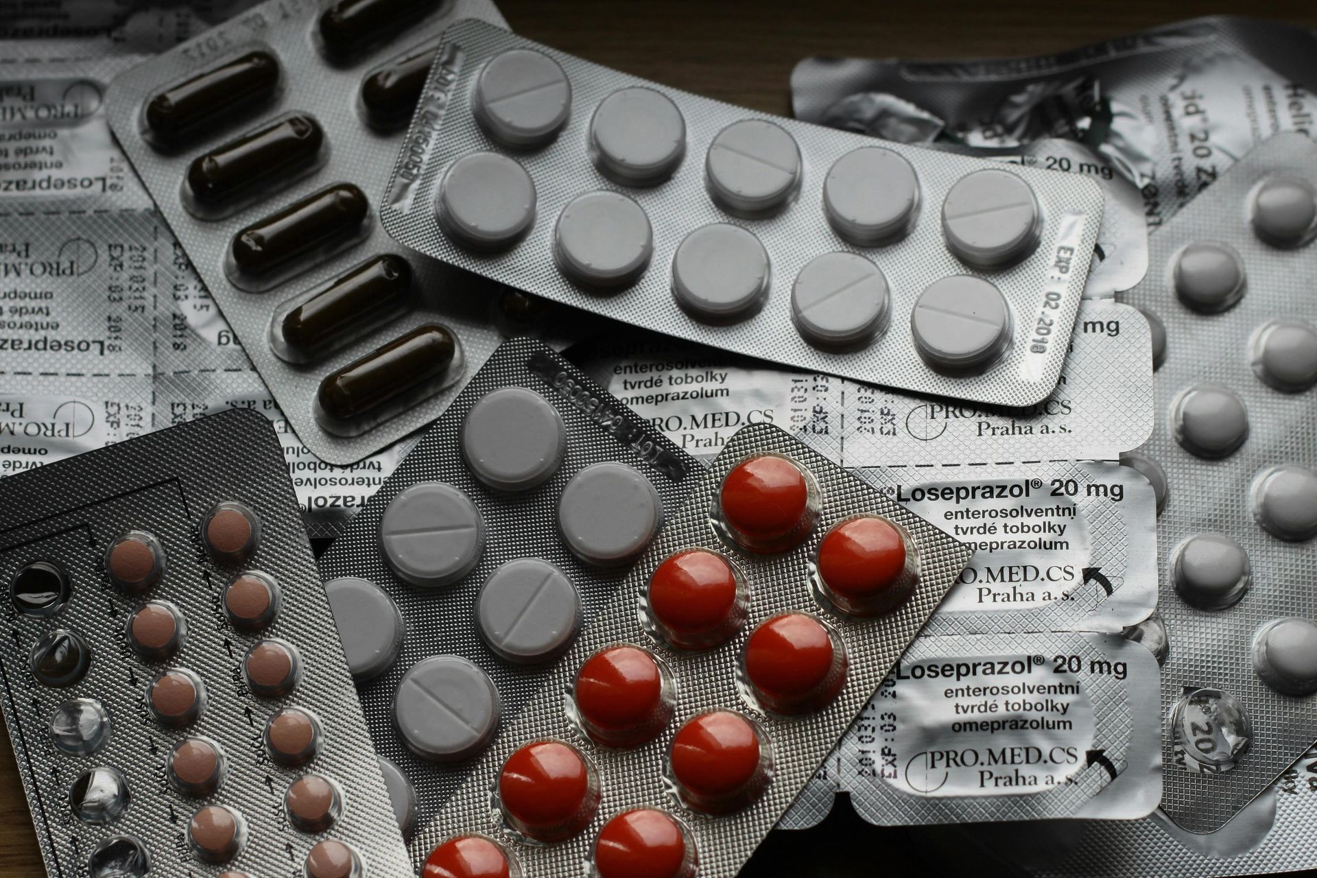 Assorted blister packs of red and gray pills on newspaper