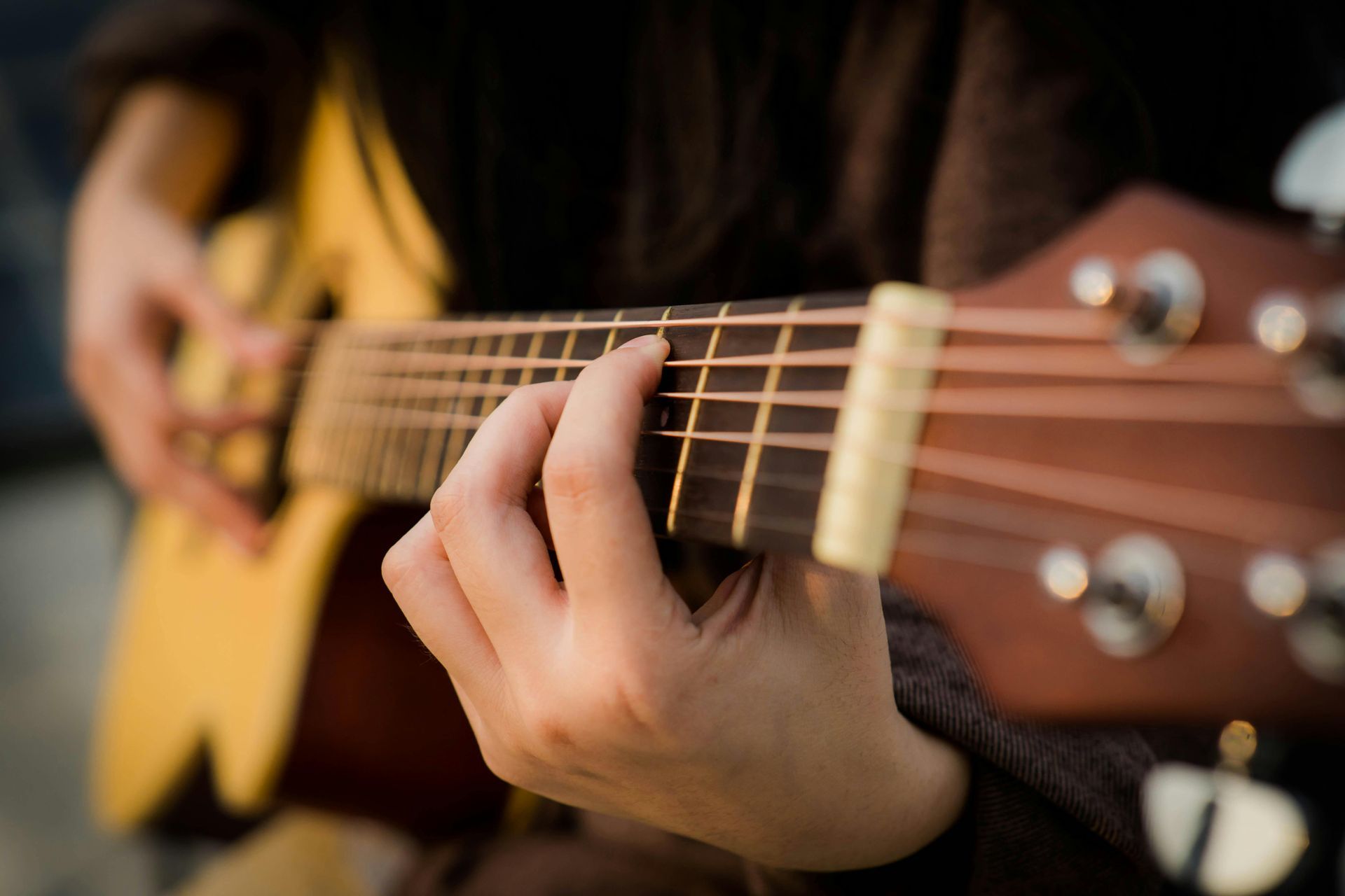 Close-up of hands playing an acoustic guitar, with fingers pressing the strings near the fretboard.