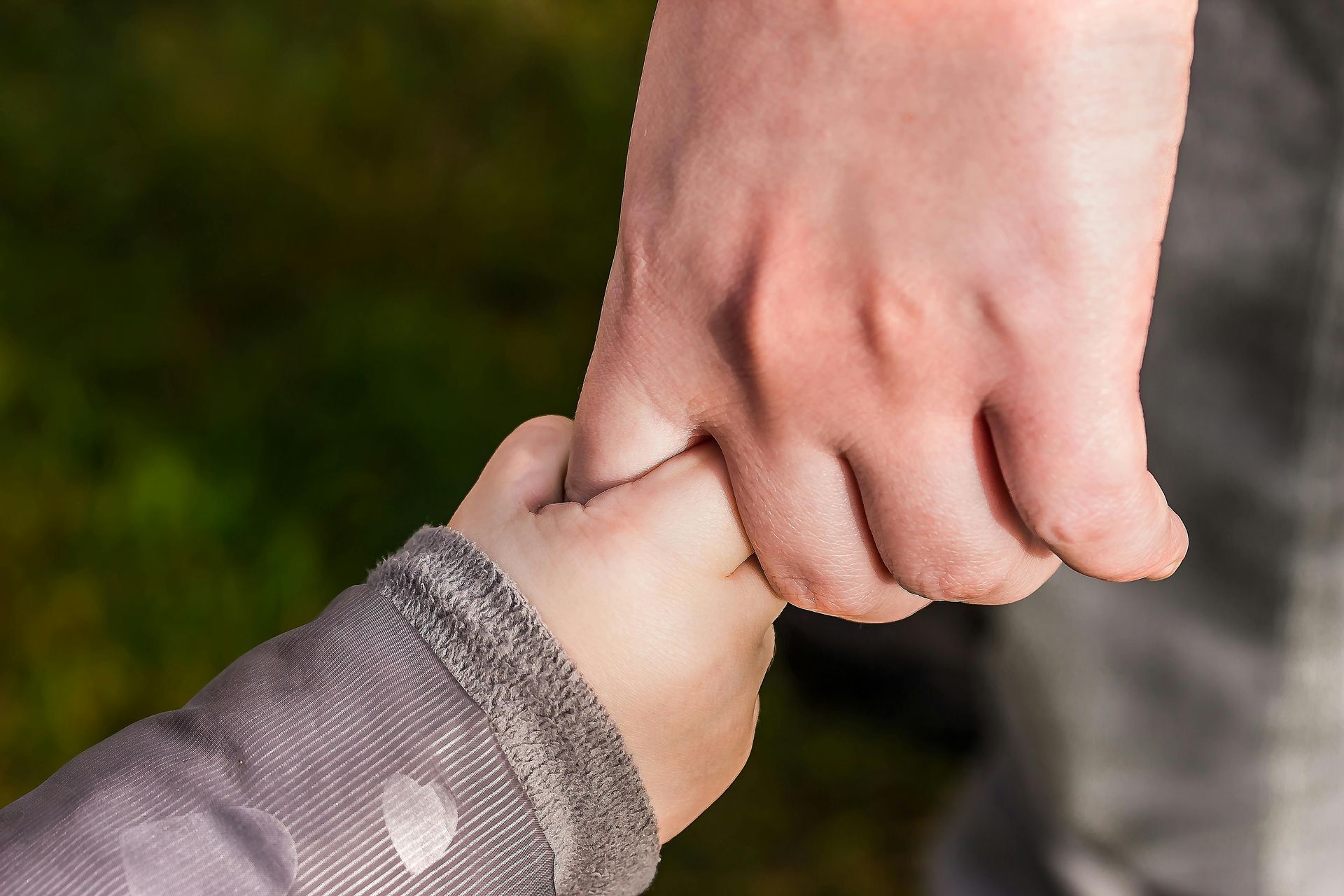 Adult hand holding a baby’s hand outdoors