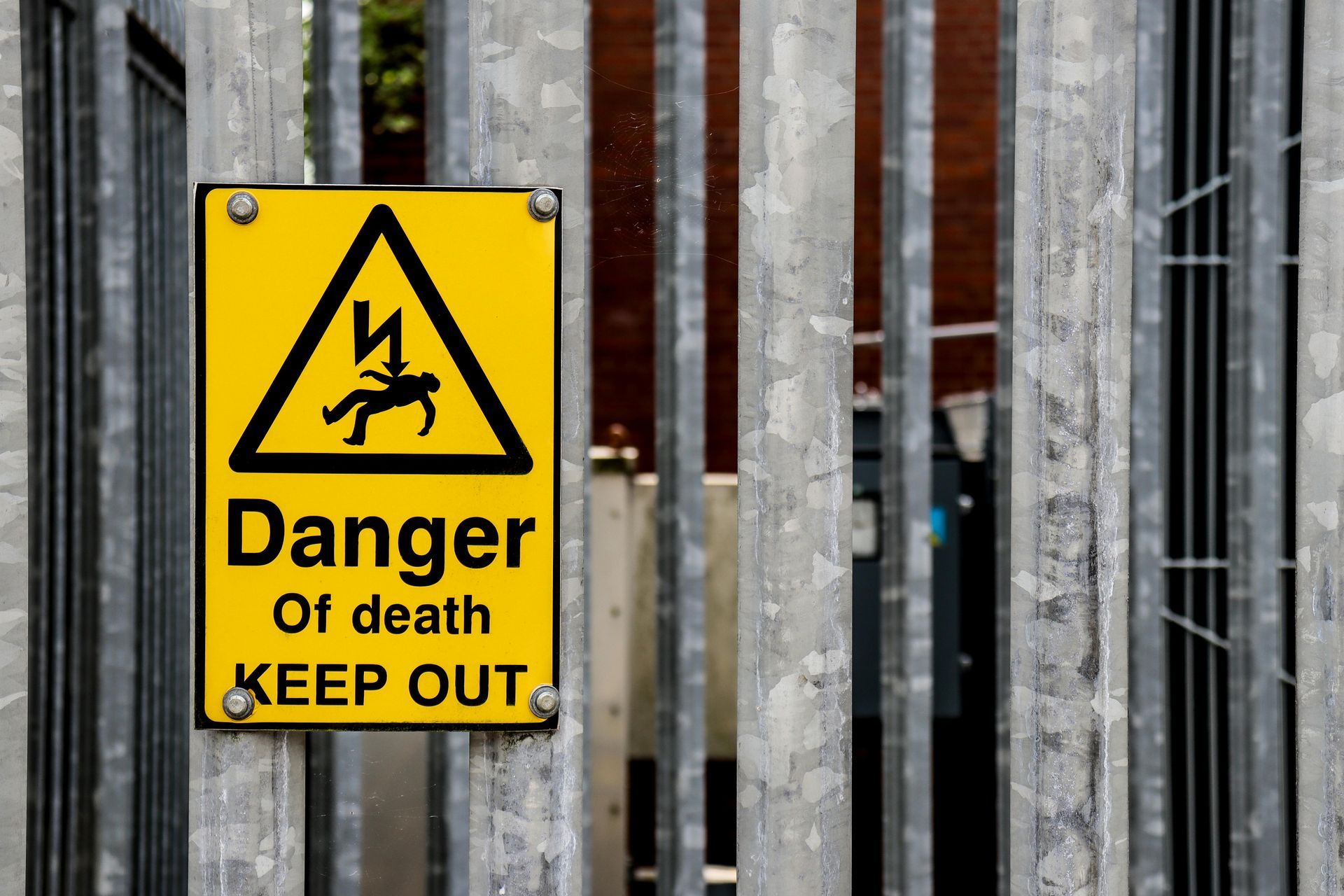Yellow warning sign on a metal fence reads “Danger of death, keep out.”