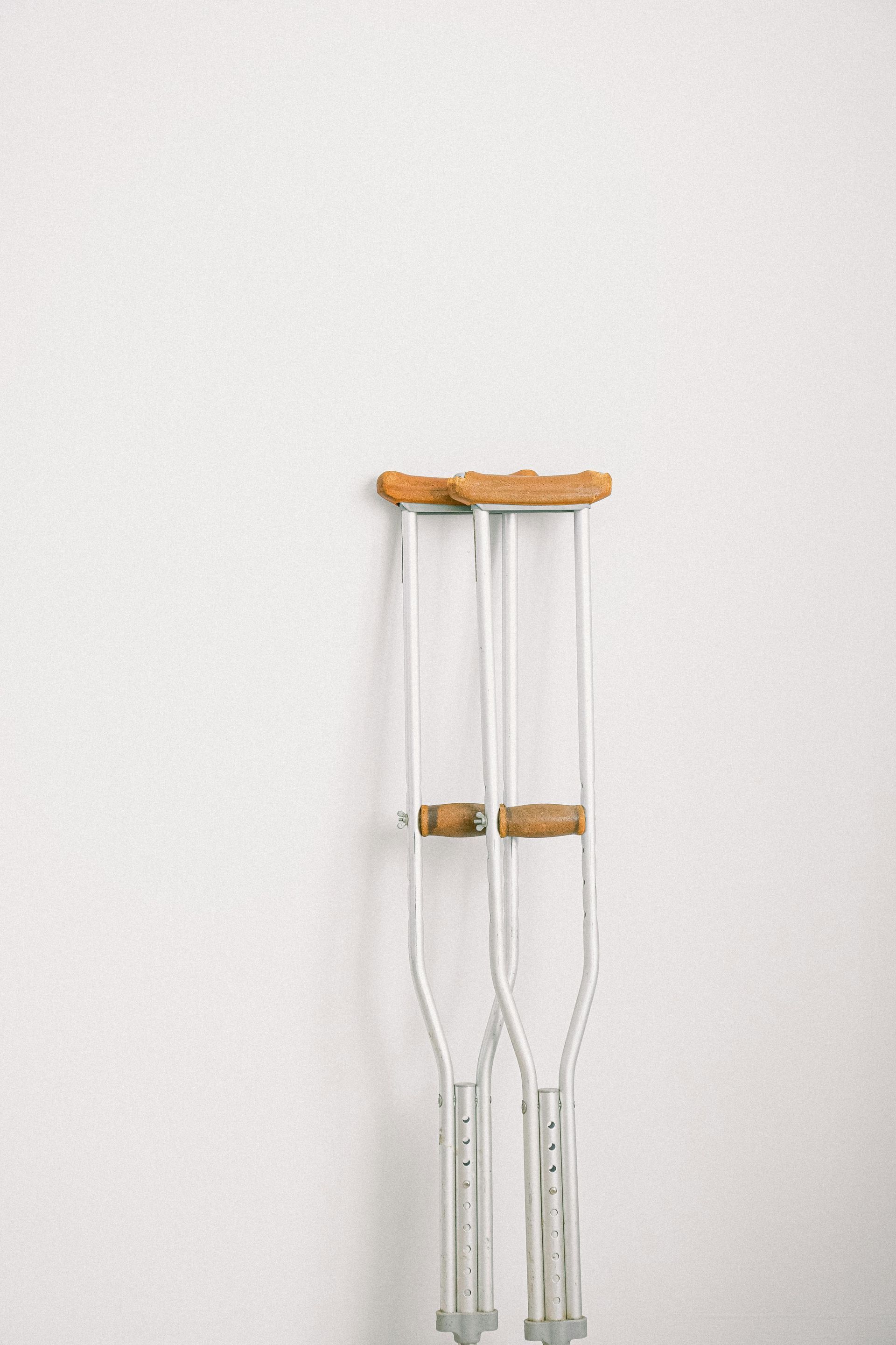 Two clear crutches with orange handles leaning against a white wall