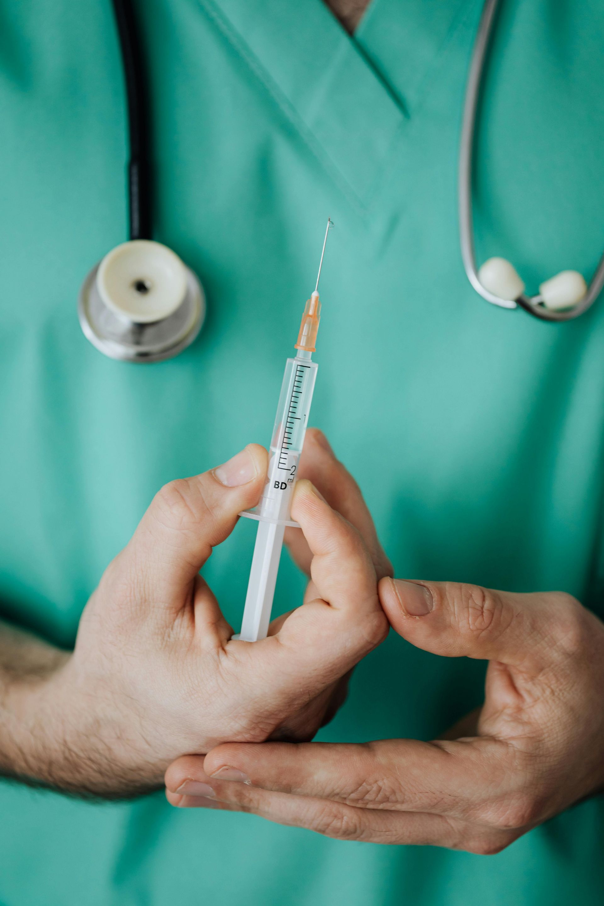 Healthcare worker holding a syringe against a teal scrubs background