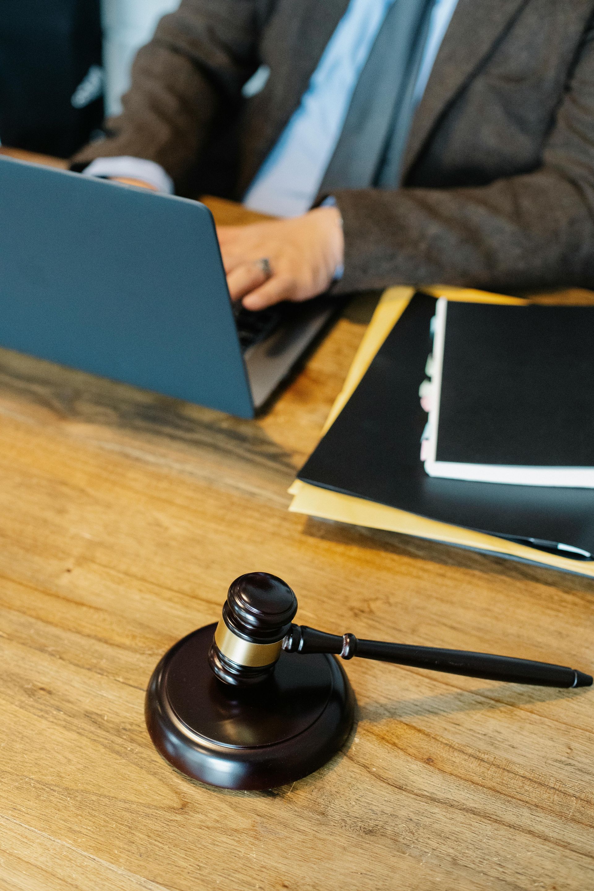 Judge’s gavel on a wooden desk beside a laptop and paperwork in a meeting or courtroom setting