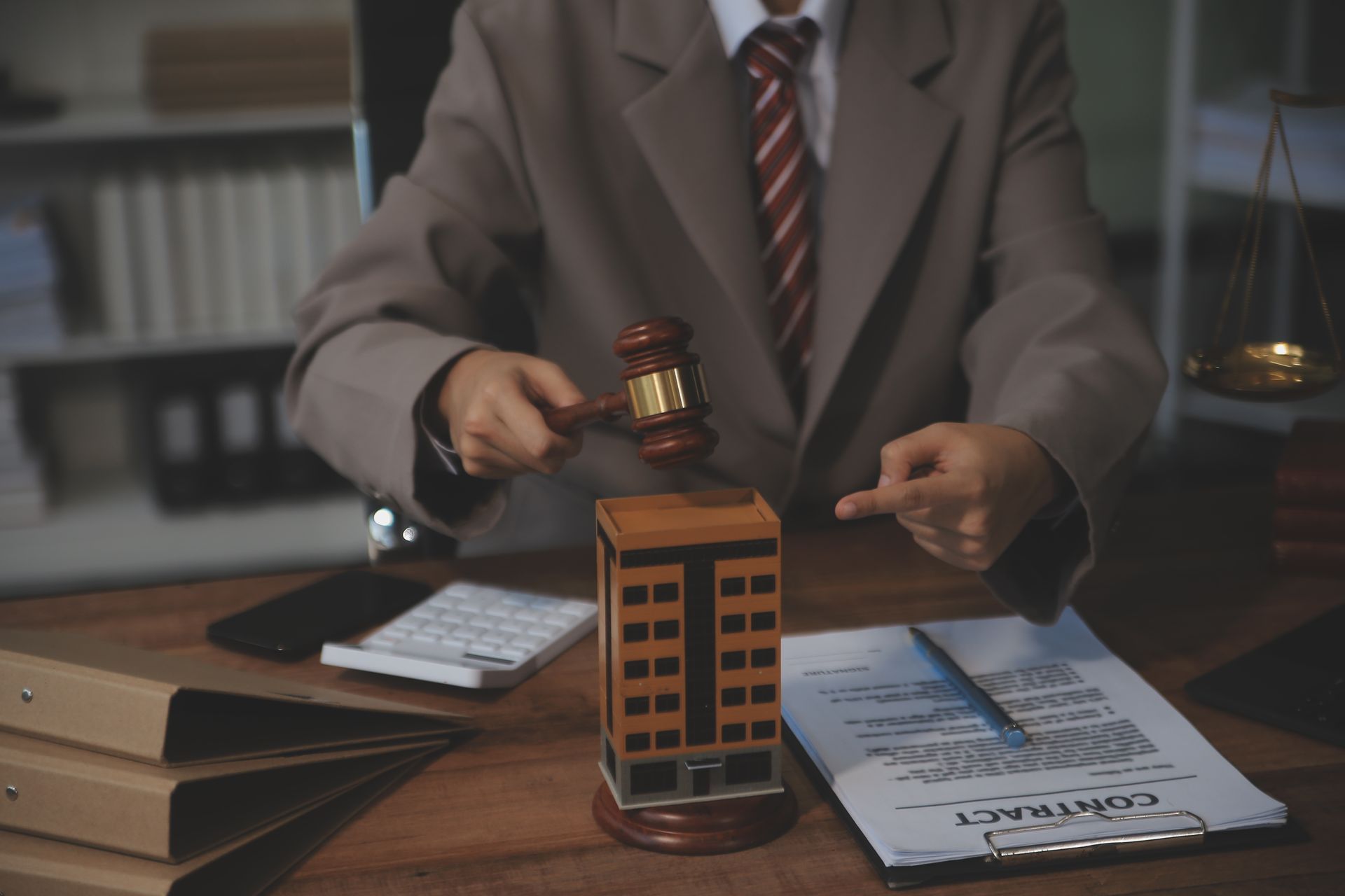 Lawyer in suit striking a gavel at desk with documents and a calculator in a courtroom office