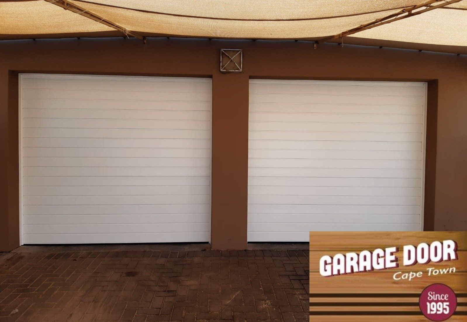 White garage doors on a brown wall, beneath a brown canopy.