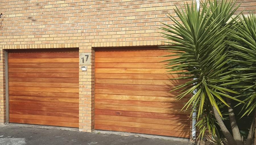 Two wooden garage doors with brick facade, address number 17, and a green plant.