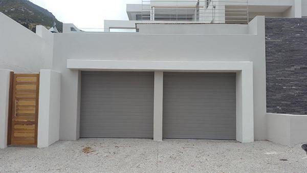 Two gray roll-up garage doors in a white frame, next to a wooden gate.
