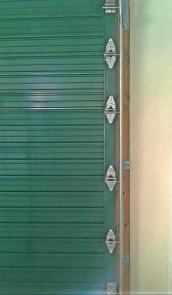 Green garage door with four hinges, next to a beige wall and wood trim.