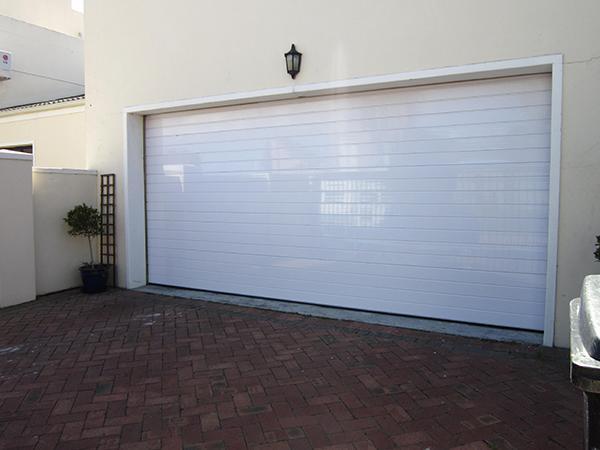 White garage door on a brick driveway, with a light fixture above.