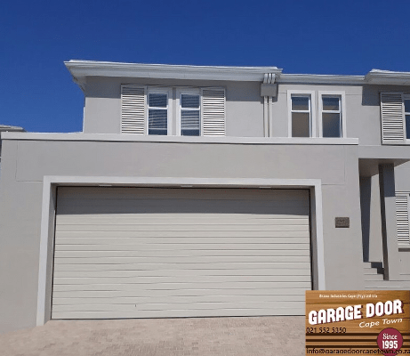 Garage door in a light gray house with matching shutters against a blue sky.
