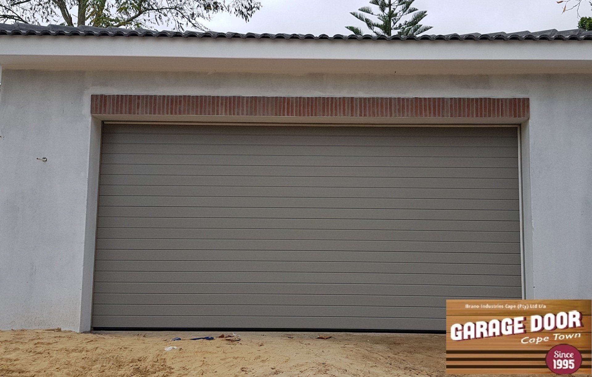 Gray garage door in a light-colored building, with a brick accent above.