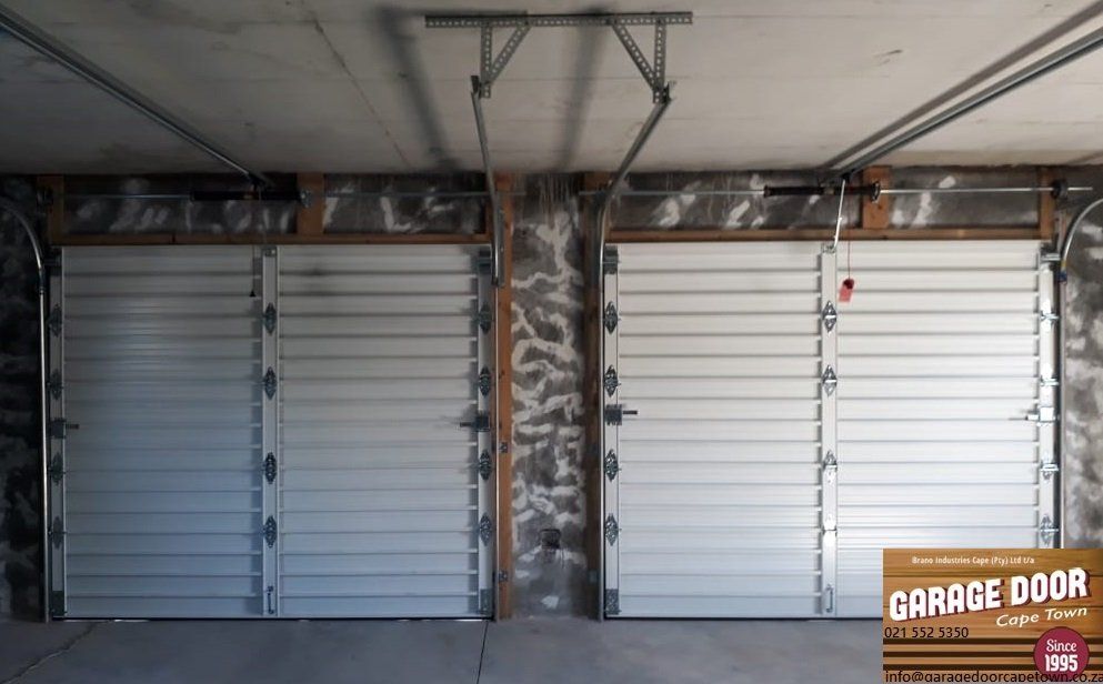 Two white horizontal-slat garage doors side-by-side; one door is open slightly. Beige walls.