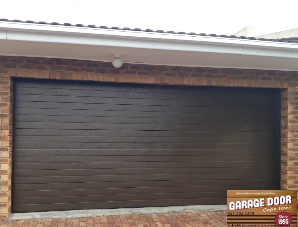 Brown horizontal-panel garage door on a brick building, with a brown sign in the bottom corner.