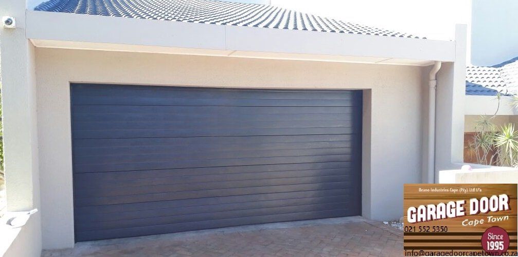 A gray garage door on a beige house. A wooden sign for 