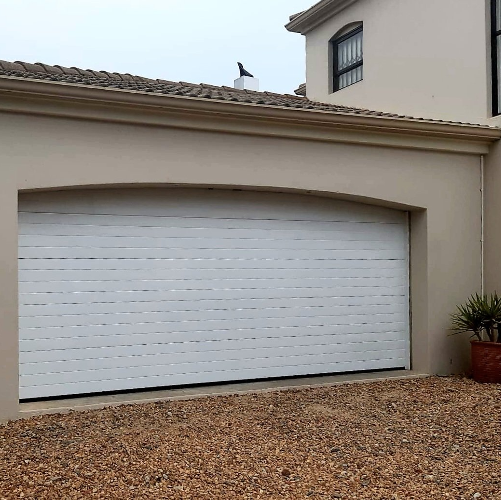 White rolling garage door on a beige building. A bird sits on the roof.