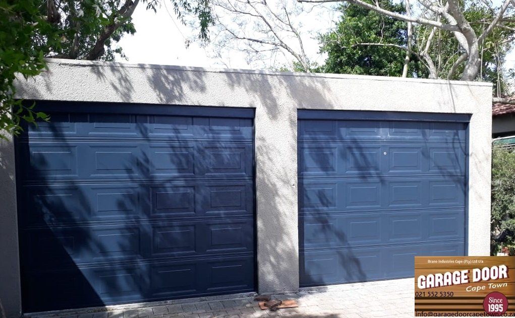 Two blue garage doors in a concrete building with trees in the background.