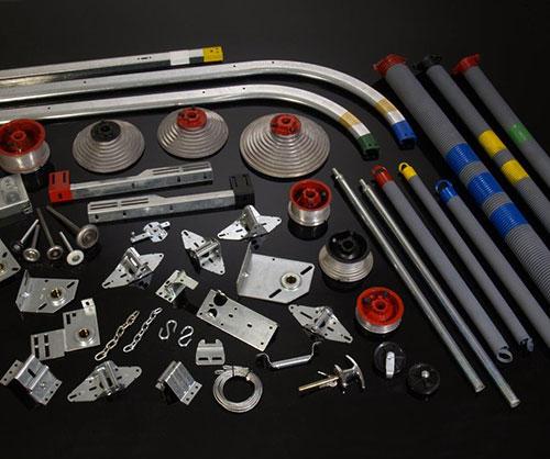 Garage door parts and components laid out on a black surface, including springs, tracks, and mounting hardware.