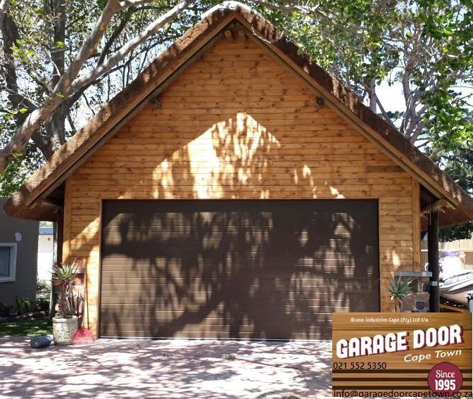Garage with a brown garage door and thatched roof, set in a driveway.