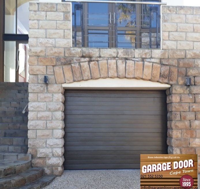 Brown garage door framed by stone arch and brickwork, leading to a building facade.