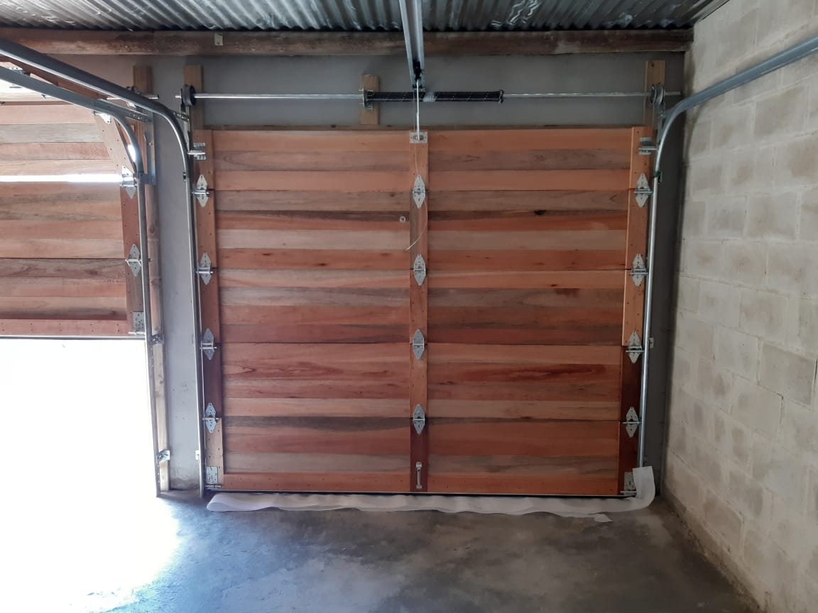 Wooden garage door, partially closed. Interior view. Beige brick walls, grey concrete floor.